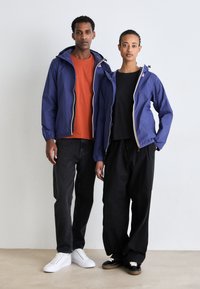 Purple lightweight jackets with elastic cuffs, worn over a black and orange shirt. Black and gray pants, white and black sneakers.