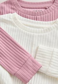 Trois hauts côtelés : un rose clair, deux blancs. Les hauts présentent des encolures rondes et un tissu texturé avec des coutures et des poignets visibles.