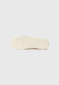 Cream-colored sneaker sole with a textured zigzag pattern. The material appears rubberized and smooth with rounded edges.