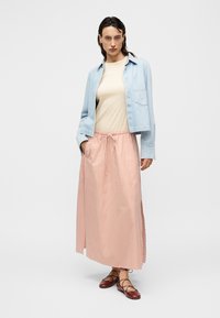 Φωτεινό γαλάζιο τζιν μπουφάν, μπεζ μπλουζάκι και μακρύ κόκκινο και άσπρο ριγέ φούστα. Καφέ δερμάτινα παπούτσια με κορδόνια και επίπεδη σόλα. Καθημερινή εμφάνιση με άνετη εφαρμογή.