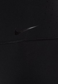 Černé sportovní legíny z hladkého materiálu s nenápadným logem Nike a malými perforacemi pro ventilaci.
