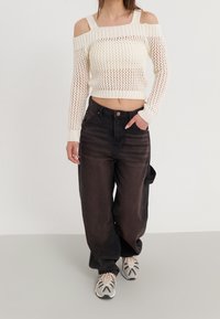 Ivory, dzianinowy sweter crop z dekoltem na ramionach; czarne, szerokie dżinsy; beżowe sneakersy z granatowymi akcentami; widoczne teksturowane detale.