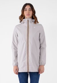 Giacca impermeabile grigia chiara con cappuccio, cerniera completa e polsini elasticizzati. Presenta una striscia colorata sul davanti e due tasche laterali.