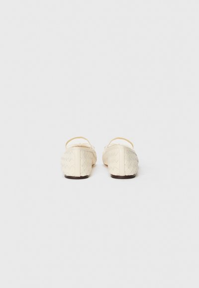 Pantofi plat țesuți de culoare crem, cu un design deschis, având curele subțiri și o suprafață texturată. Talpă plată, flexibilă, cu un hardware minim.