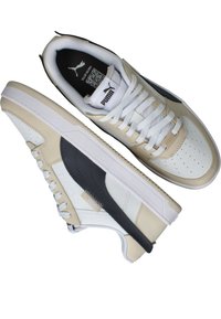 Tan en witte sneakers met een gestructureerde leren bovenkant, voorzien van grijze accenten, platte witte veters, een merklabel op de tong en een rubberen zool.