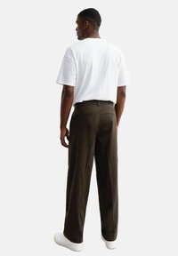 Pantalons marron à jambes larges avec une texture lisse, associés à un t-shirt blanc uni, portés avec des baskets blanches. Poches arrière visibles.