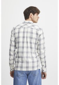 White plaid shirt with gray and navy check pattern, buttoned cuffs, and a classic collar. Worn with blue jeans, showing back view.