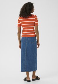Haut en tricot à manches courtes, rayé orange et blanc, assorti à une longue jupe en denim. La tenue est complétée par des sandales noires à enfiler.