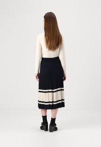 Jupe midi plissée marine et crème avec une large ceinture ; caractérisée par des rayures horizontales et un tissu texturé. Portée avec des chaussures à talons carrés.