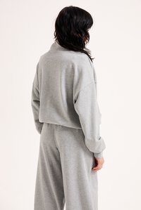 Γκρι φούτερ και αντίστοιχα φόρμα, κατασκευασμένα από μαλακό ύφασμα. Κ�οντό σχέδιο με κατεβασμένους ώμους και χαλαρή εφαρμογή. Λείο υλικό.