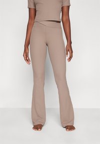 Leggings évasés côtelés beige avec une taille haute croisée, associés à un crop top assorti. Les deux sont fabriqués en tissu extensible.