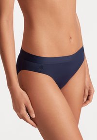 Tumed sinine bikiinipõhi sileda tekstuuri ja elastse vöökohtaga, millel on külgedel peenelt sissepressitud logo detail.