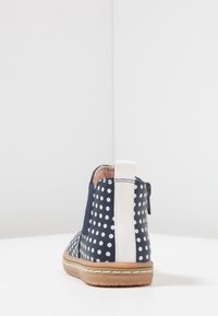 Botte cheville bleu marine avec des pois blancs, une rayure verticale blanche sur le talon et une semelle marron clair sur une surface blanche.