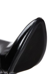 Chaussure en cuir synthétique noir avec un bout pointu et une semelle en caoutchouc texturée. Elle présente une finition brillante et un design élégant.