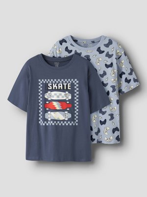 Deux T-shirts pour enfants à manches courtes : un bleu foncé avec un motif de skateboards et le texte "SKATE", un bleu clair avec un motif sombre de manettes de jeu.