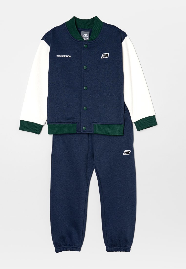 Un survêtement deux pièces comprend un hoodie bleu marine avec des manches blanches, des accents verts, des boutons-pression et un pantalon bleu marine assorti avec des poignets élastiques.