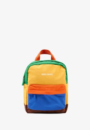 Zainetto piccolo con parte superiore verde, fronte giallo, pattina della tasca arancione, tasca blu e base marrone, con il testo "BOBO CHOSES" sul davanti.