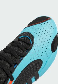 Chaussure de sport avec une tige synthétique bleue et noire, dotée d'une texture perforée, des lacets noirs et des accents rouges vifs sur la semelle.