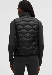 Musta, tikattu untuvatakki, jossa on korkea kaulus ja hihaton muotoilu, sileä pinta ja joustava helmaring, joka takaa tiukan istuvuuden.