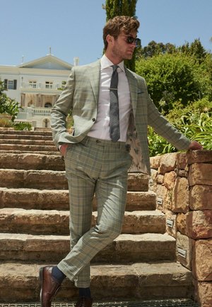 Světle zelený kostkovaný oblek s slim fit střihem a strukturovanou tkaninou. Stylizovaný s bílou košilí, šedým kravatou a hnědými koženými botami.