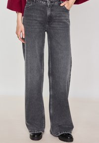 Jeans à jambes larges et taille haute en denim noir délavé. Présente une couture contrastée et un design classique à cinq poches. Texture lisse.