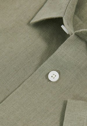 Olívovo zelená ľanová košeľa s bielym gombíkom a ostrým golierom, s textúrovanou tkaninou, ktorá ukazuje jemné detaily väzby.