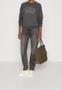 Felpa grigia con "GAP" in strass, abbinata a jeans neri sbiaditi, scarpe da ginnastica bianche e una borsa a tracolla in suede verde scuro.