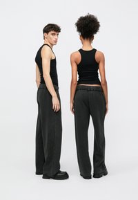 Musta t tankkitoppi ja hiilenharmaat leveälahkeiset housut, joissa on joustava vyötärönauha ja teksturoitu kangas. Asusteisiin kuuluvat massiiviset mustat kengät.