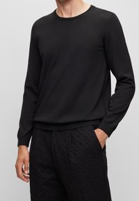 Schwarzer langärmliger Rundhalsausschnitt-Pullover aus glattem Strickstoff, mit gerippten Bündchen und Saum, kombiniert mit schwarzen strukturierten Hosen.