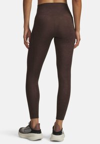 Woman wearing dark brown high-waisted leggings and mauve and gray athletic shoes, standing with back facing forward.