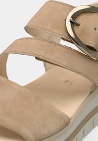 Μπεζ σουέντ σανδάλι με δύο φαρδιές λουρίδες, κυκλικό μεταλλικό πόμολο και υφασμένο λευκό πέλμα με αυλακώσεις για καλύτερο κράτημα.