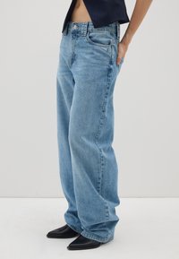 Jeans larghi azzurri chiari in denim, con cinque tasche, chiusura con bottone superiore e orli sfrangiati. Abbinati a stivali neri con punta.