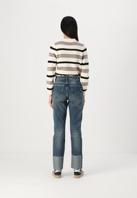 Striped sweater in cream, gray, and black, paired with faded blue jeans featuring a cuffed hem and distressed details. Back view.