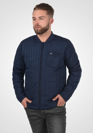 Chaqueta bomber acolchada en color marino con cremallera frontal, cuello de canalé y un bolsillo en el pecho. Presenta costuras verticales sutiles y mangas largas.