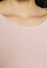 Ljusrosa, lös passform t-shirt med rund halsringning. Tyget verkar mjukt och något strukturerat med slitna kanter längs sömmarna.