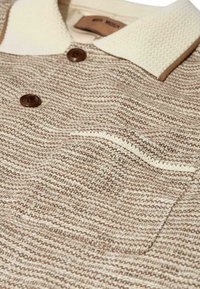 Beige and brown woven polo shirt with cream knit collar, two dark buttons, and a chest pocket with cream trim.