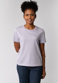 Lichtpaarse katoenen t-shirt met korte mouwen, een ronde halslijn en een tekstprint op de voorkant. Gecombineerd met donkerblauwe jeans.