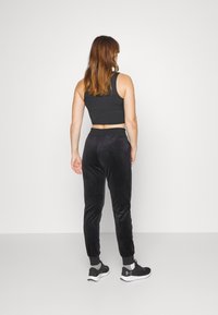 Zwarte velours joggers met taps toelopende pijpen, een elastische tailleband en geribbelde enkels, gecombineerd met een aansluitend zwart crop topje en zwarte sneakers.