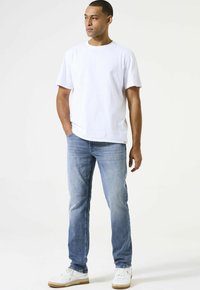 Camiseta de algodón blanca, con cuello redondo y mangas cortas; combinada con unos jeans de mezclilla azul claro; zapatillas blancas con acentos beiges.