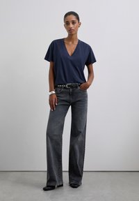 Camiseta de cuello en V de color navy, de corte relajado, combinada con jeans grises de pierna ancha de tiro alto. Cinturón negro con herrajes plateados, textura suave, líneas limpias.