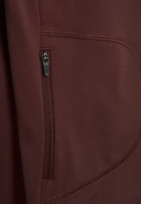 Körsbärsfärgad jacka med en dragkedjeficka, jämn textur och synliga sömnadsdetaljer, med en figurnära design för komfort och funktionalitet.