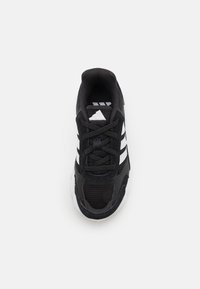 Zapatilla deportiva negra con material de malla y sintético, suela de goma, cordones y tres franjas blancas en el lateral.