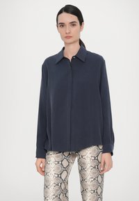 Camisa navy de botones con cuello, mangas largas y un ajuste relajado, combinada con pantalones metalizados de estampado de serpiente que presentan un patrón texturizado.
