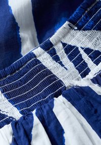 Sininen ja valkoinen kuviollinen kangas, jossa on poimutettu rakenne. Syvän siniset yksityiskohdat ja sujuva, virtaava muotoilu. Materiaali vaikuttaa kevyeltä ja hengittävältä.