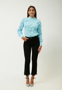 Maglione lavorato a maglia blu chiaro con motivi floreali, colletto alto e maniche lunghe, abbinato a jeans neri a vita alta e tacchi appuntiti argentati.