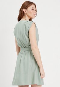 Robe vert clair avec des manches courtes bouffantes, taille ceinturée et jupe évasée. Fabriquée en tissu doux avec une texture lisse.