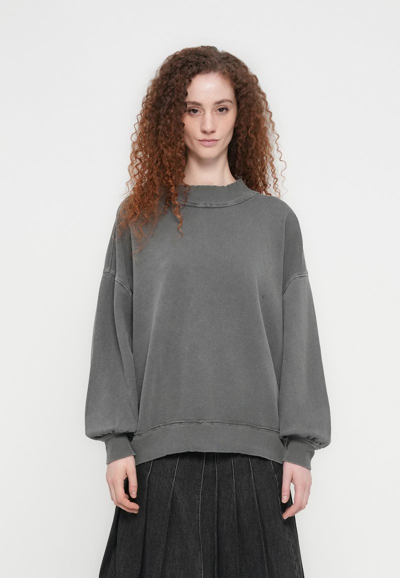 Γκρι φαρδιά φούτερ από απαλό ύφασμα, με ριμπ λαιμόκοψη, χαμηλωμένους ώμους και μανίκια με μανσέτες. Συνδυασμένο με πλισέ μαύρη φούστα.