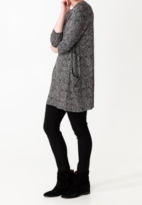 Túnica de cachemira en blanco y negro con mangas tres cuartos, combinada con pantalones ajustados negros y botas de tobillo. Tejido suave con bolsillos laterales.