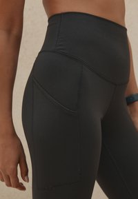 Leggings negros con una cintura alta, que cuentan con un bolsillo lateral y costuras en contraste. Textura suave, diseñados para brindar comodidad y flexibilidad.