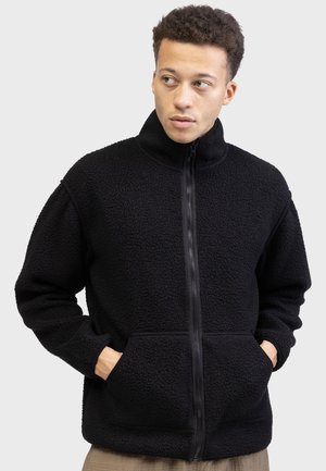 Black fleece jacket with a high collar, front zipper, and two side pockets. Textured fabric with a soft finish and relaxed fit.